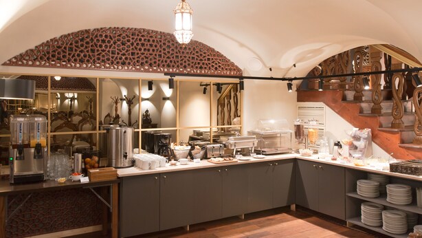 A spacious kitchen with a high ceiling, a decorative wooden ceiling, and a central chandelier. - Hotel Karlin (Prague)