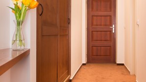 A hallway with a wooden door at the end, a wooden wardrobe, and a vase with flowers on a shelf. - Hotel Karlin (Prague)