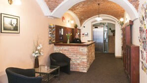 A reception area with a stone counter, a receptionist, a black armchair, a glass table, and a brick ceiling. - Hotel Karlin (Prague)
