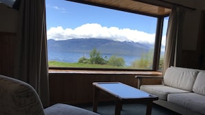 A room with a sofa, a small table, and a view of a lake with mountains in the background. - Cabanas y Piscina Rucamalen (Puerto Varas)
