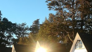 A row of white cottages with triangular roofs, surrounded by trees and a grassy area. - Cabanas y Piscina Rucamalen (Puerto Varas)