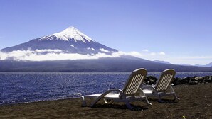 Two beach chairs facing a mountain with a snow-capped peak and a body of water. - Cabanas y Piscina Rucamalen (Puerto Varas)