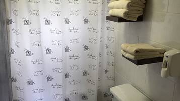 A bathroom with a toilet, a sink, a towel rack with towels, and a shower curtain with text.