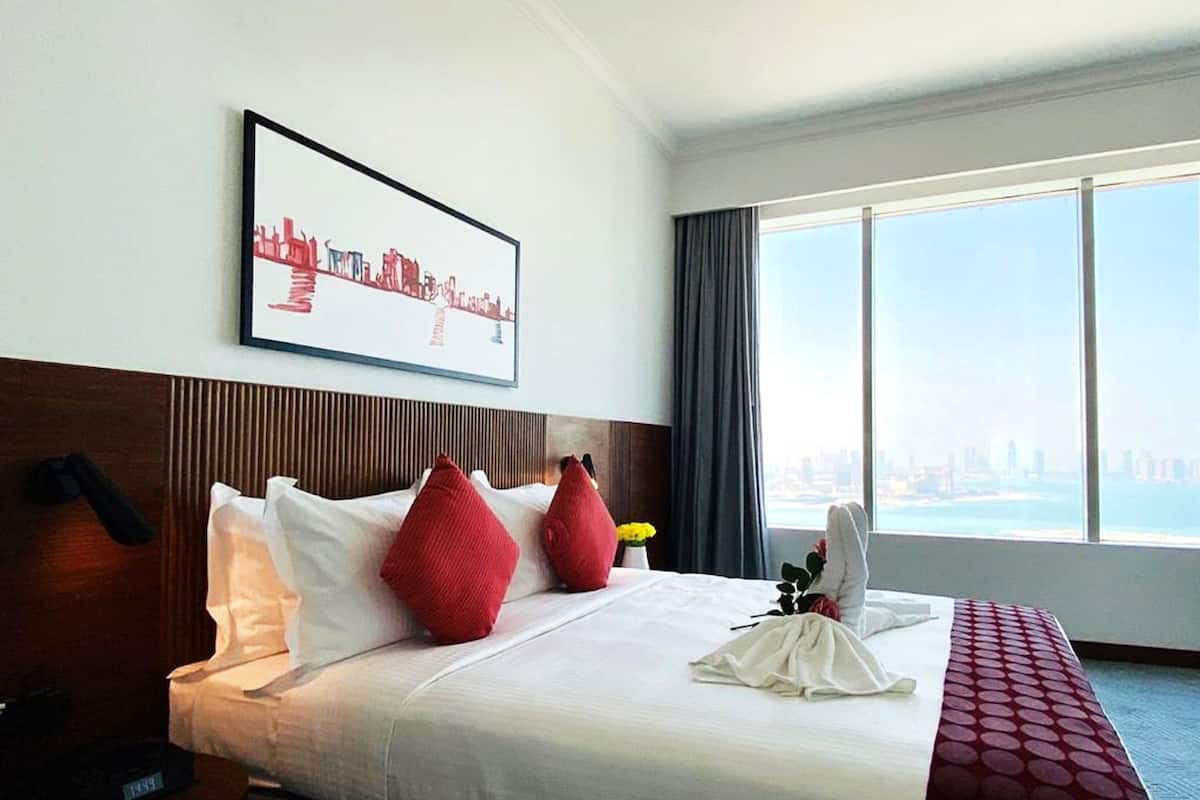 Ein Hotelzimmer mit einem großen Bett, Blick auf die Stadt, einem gerahmten Bild an der Wand und einem mit Vorhängen versehenen Fenster.