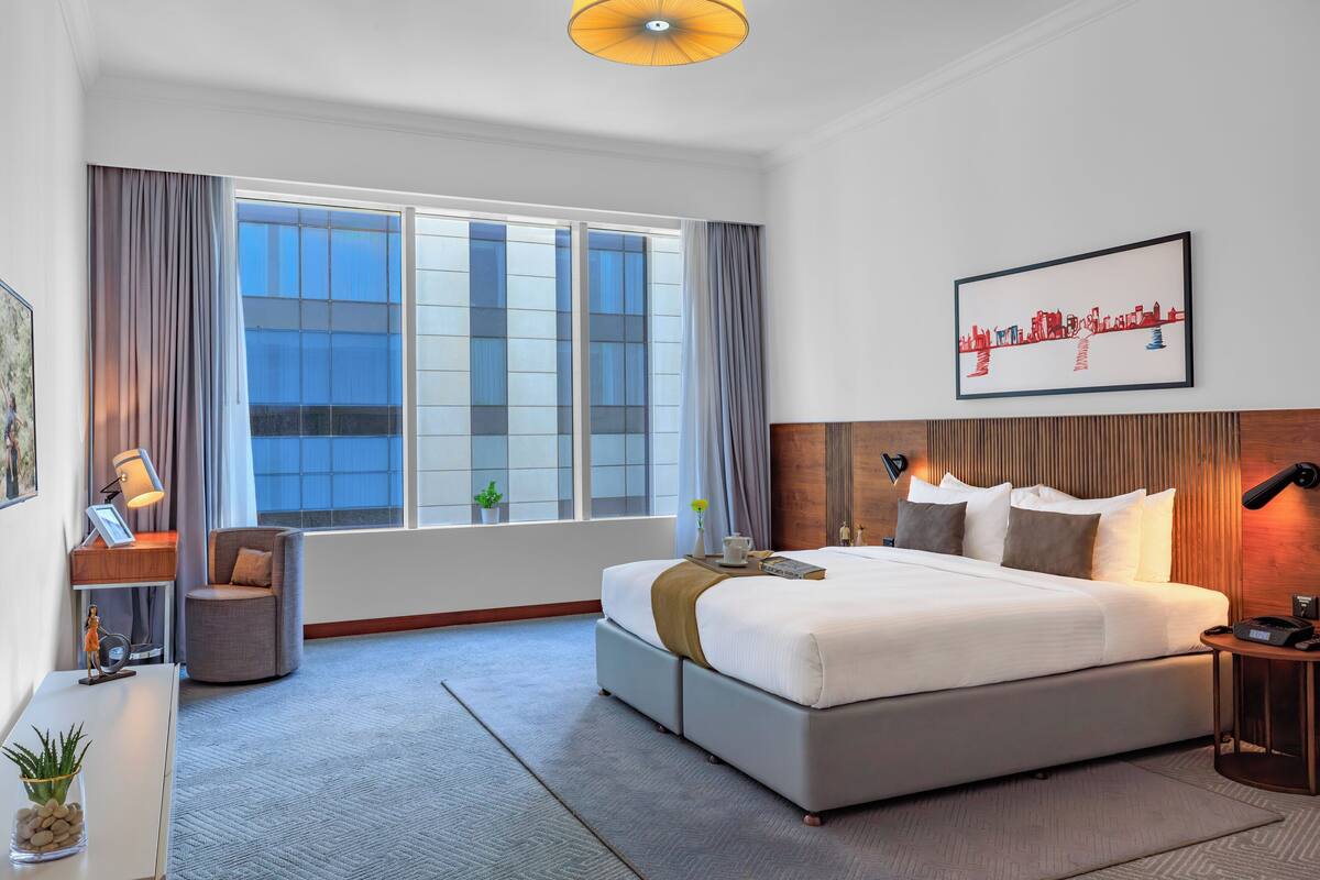 Ein modernes Hotelzimmer mit einem großen Bett, einem Schreibtisch, einem Stuhl und einem großen Fenster mit Vorhängen.