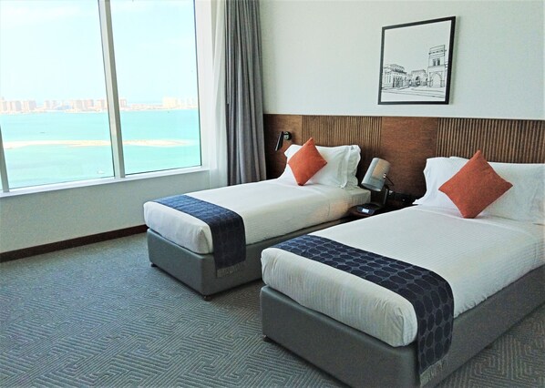 A hotel room with two beds, a view of the sea, and a framed picture on the wall.