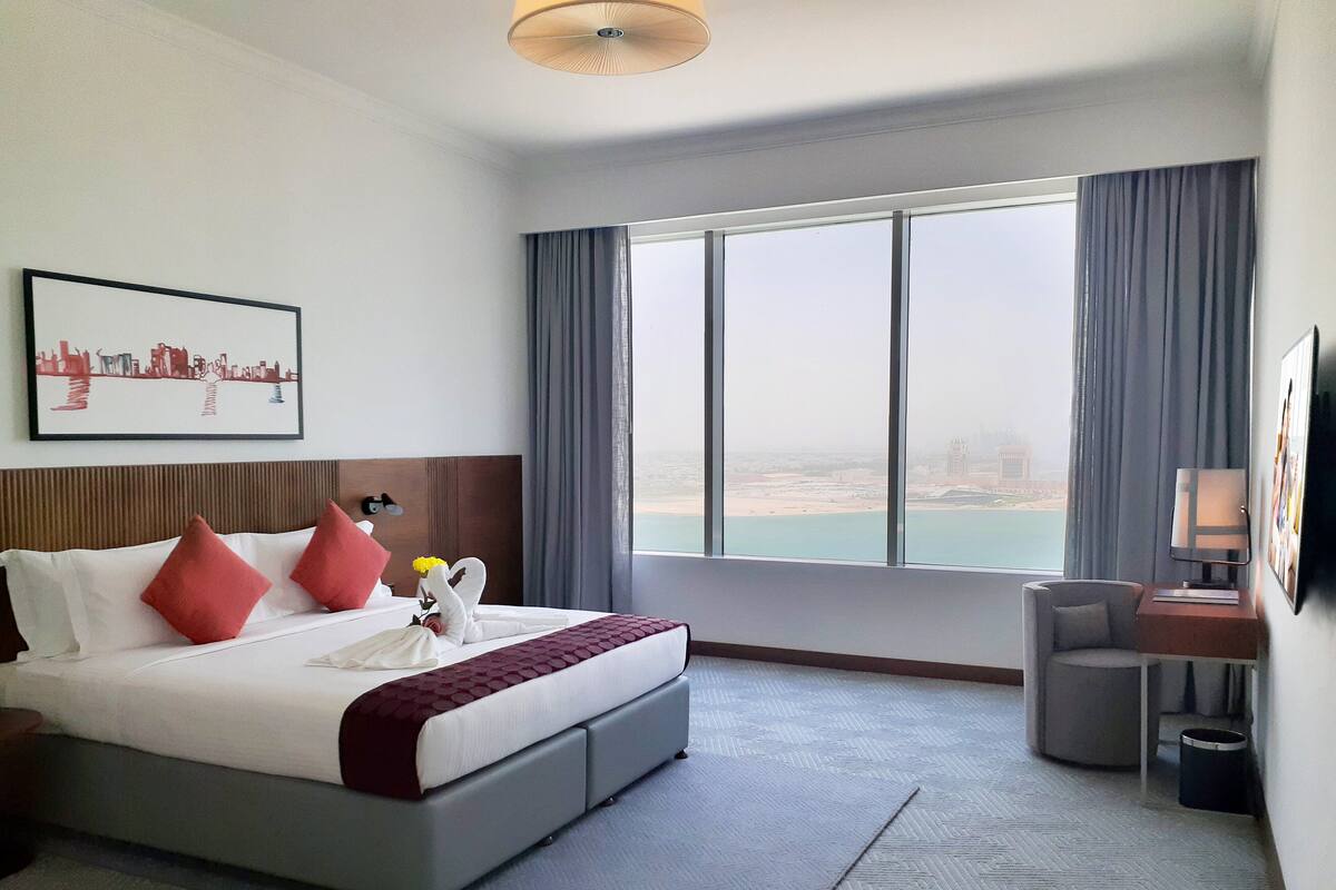 Ein Hotelzimmer mit einem großen Bett, einem Schreibtisch und Blick auf die Stadt.