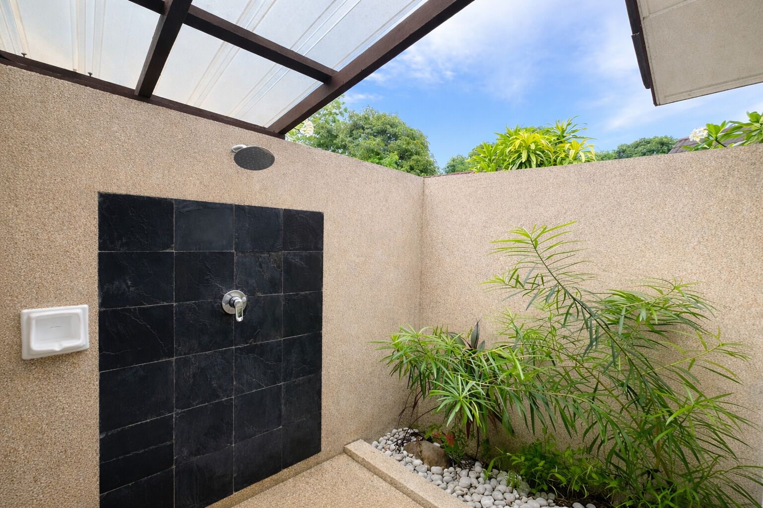 Un área de ducha moderna con pared de azulejos negros, un cabezal de ducha manual y una pequeña planta a un lado.