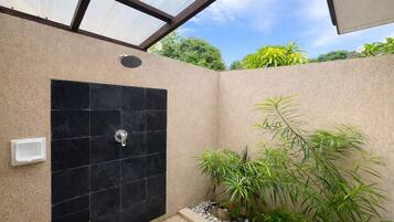 Un área de ducha moderna con pared de azulejos negros, un cabezal de ducha manual y una pequeña planta a un lado.