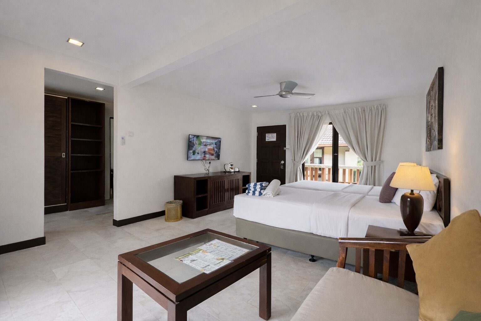 Une chambre d’hôtel équipée d’un lit, d’un bureau, d’une chaise, d’une télévision, d’un ventilateur de plafond et d’une fenêtre avec des rideaux.