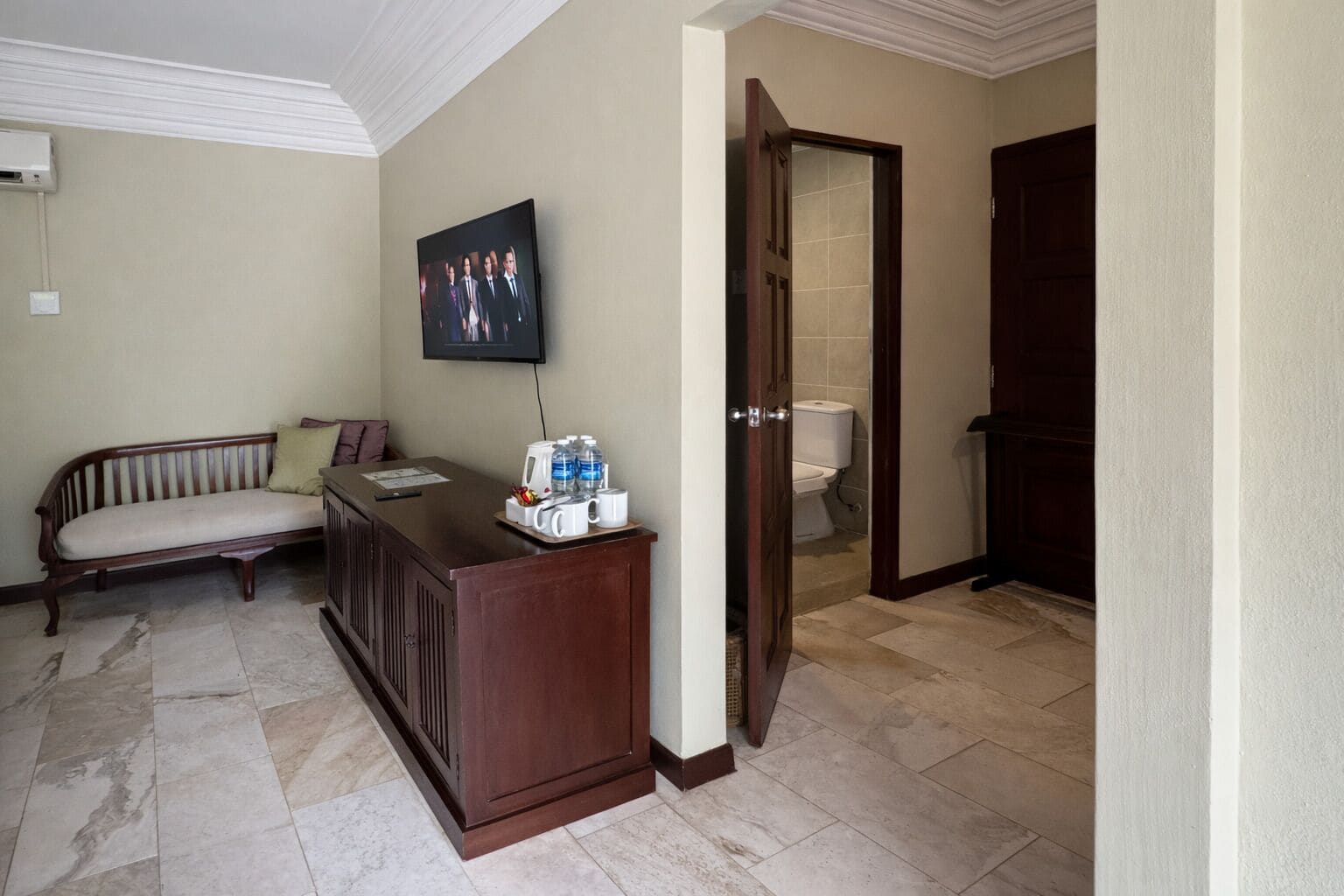 A hotel lobby with a reception desk, a bench, a television, and a door leading to a bathroom.
