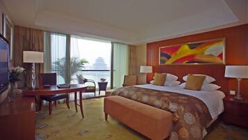 A hotel room with a large bed, a desk with a chair, a laptop, a TV, and a view of a traditional building.