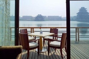 A balcony with a table and chairs, overlooking a calm body of water with traditional buildings in the background.