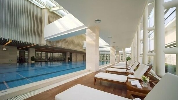 Una piscina interior moderna con sillones de descanso y un techo alto.
