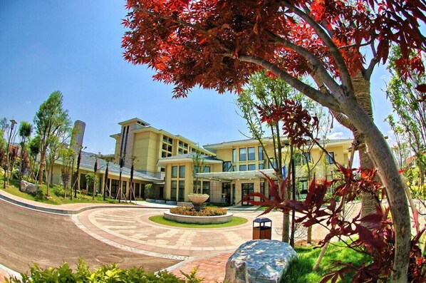 A modern hotel with a curved driveway, a central fountain, and a well-maintained garden.