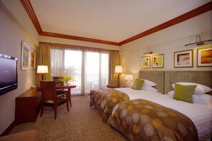 A hotel room with two beds, a desk with a chair, a TV, and artwork on the walls.