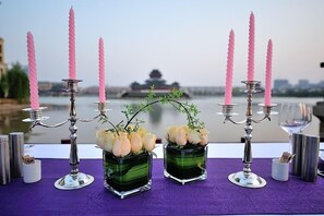 A table set with candelabras, vases with flowers, and a view of a traditional building across a body of water.