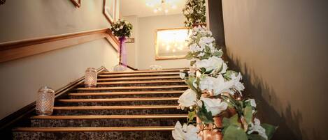 A staircase with a wooden handrail and patterned carpet, leading to a room with a chandelier and framed pictures on the walls.