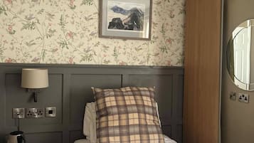 Ein Hotelzimmer mit Bett, Nachttisch, Lampe, einem gerahmten Bild an der Wand und einem Kleiderschrank.