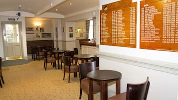 Un espace repas avec des tables et des chaises en bois, un tableau affichant le menu au mur et des tableaux encadrés accrochés au mur.