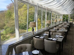 Un restaurante con una mesa larga y sillas, ventanas amplias y vistas a zonas verdes.