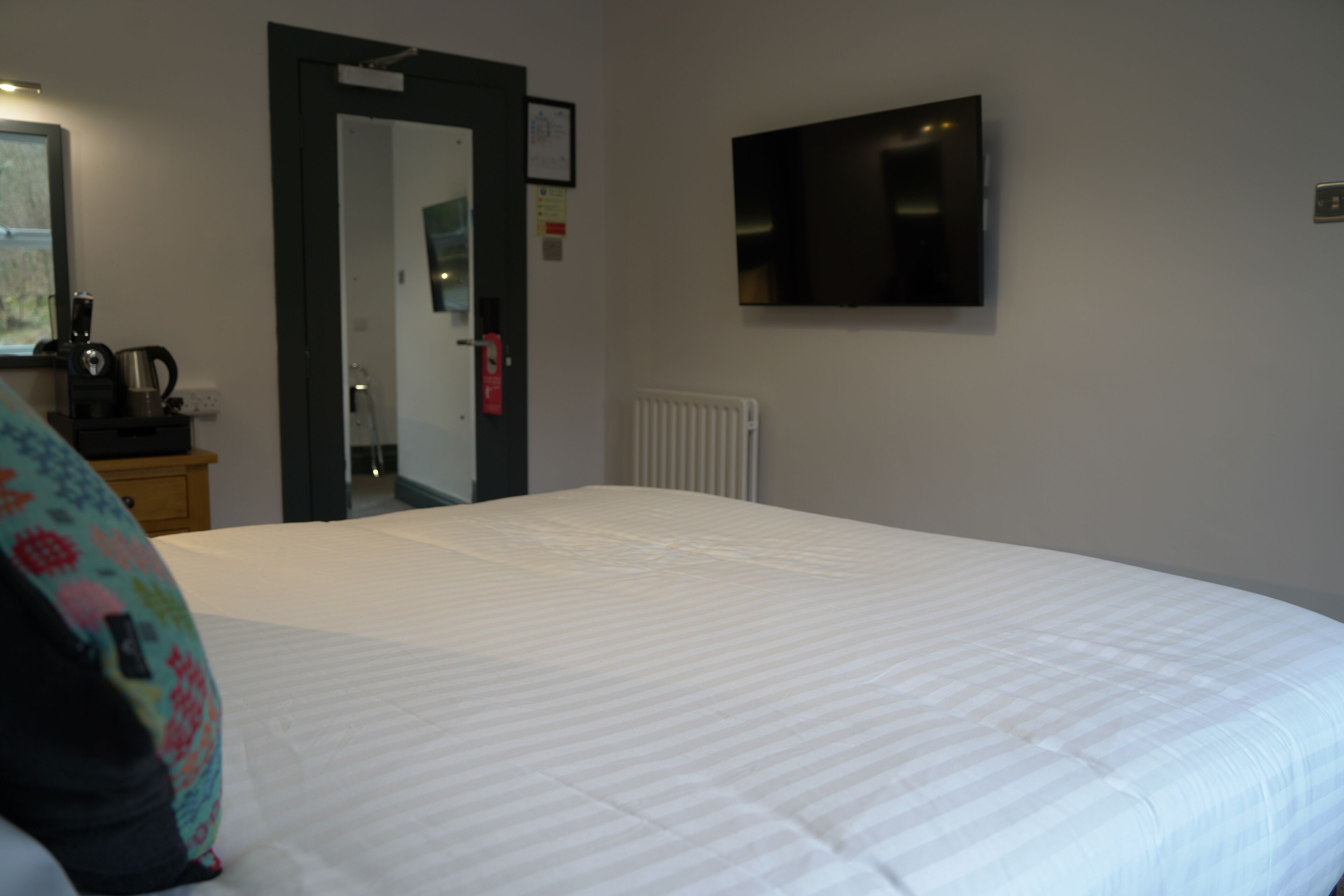 A hotel room with a large bed, a television mounted on the wall, and a radiator.