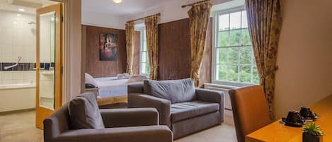 A hotel room with a bed, a sofa, a dining table, and a view of the outdoors.