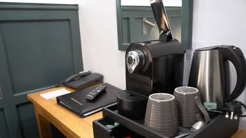 A coffee machine with a coffee pot, two cups, a remote control, and a notebook on a wooden table.