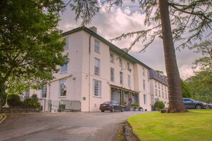 A two-story building with a symmetrical facade, a central entrance with a canopy, and a parking area in front. - The Royal Victoria Hotel (Caernarfon)