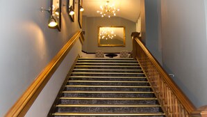 A grand staircase with marble steps and golden handrails, leading up to a landing with a chandelier and framed mirrors. - The Royal Victoria Hotel (Caernarfon)