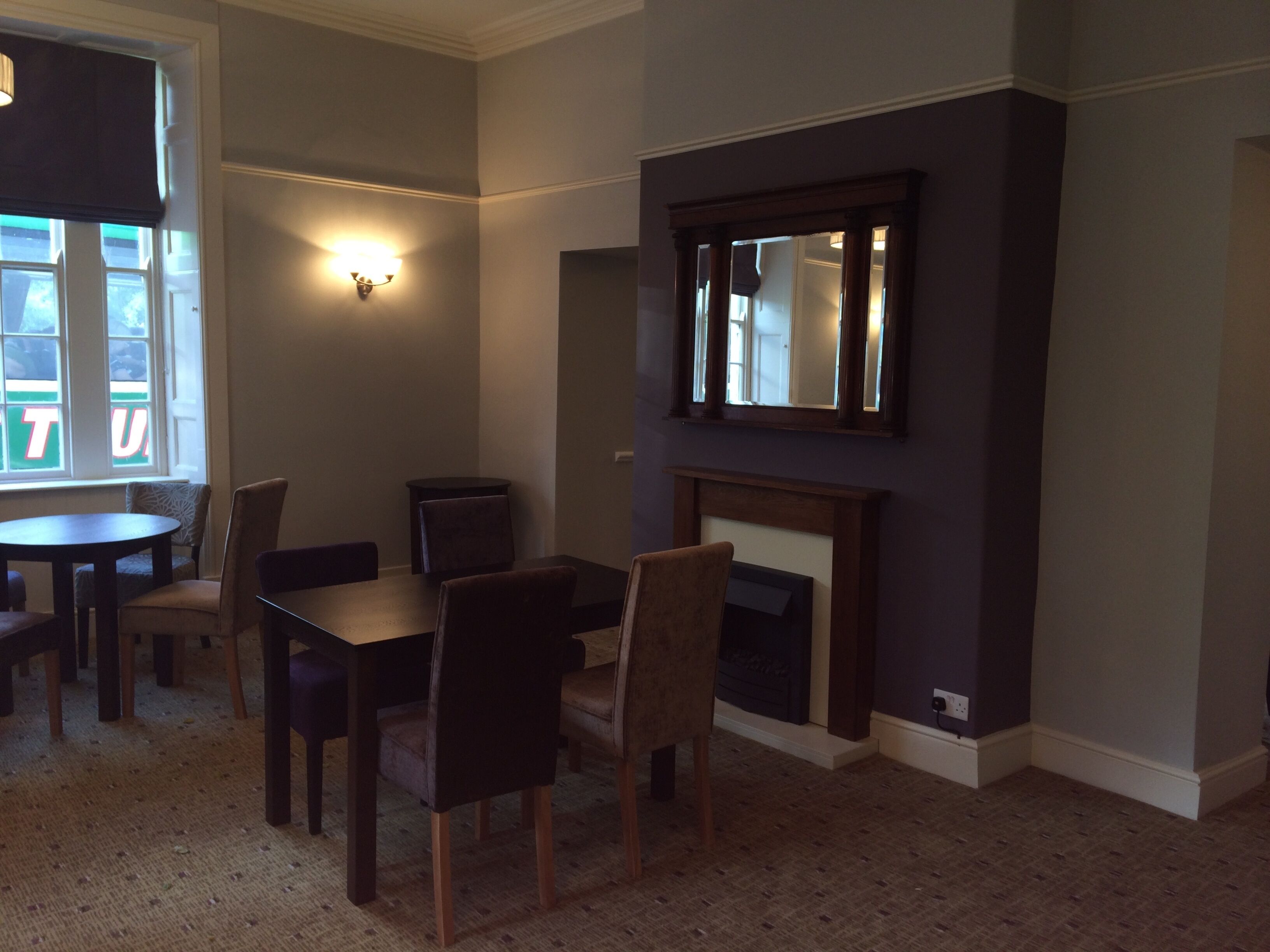 A dining area with a round table and six chairs, a wall-mounted mirror, and a fireplace.