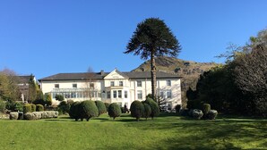 A large, two-story building with a symmetrical facade, a prominent central entrance, and a well-maintained lawn with neatly trimmed bushes and trees. - The Royal Victoria Hotel (Caernarfon)