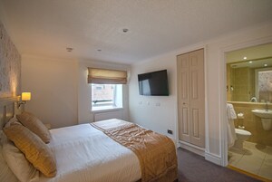 Habitación de hotel con cama, televisor montado en la pared, ventana con vistas y baño con lavamanos e inodoro.