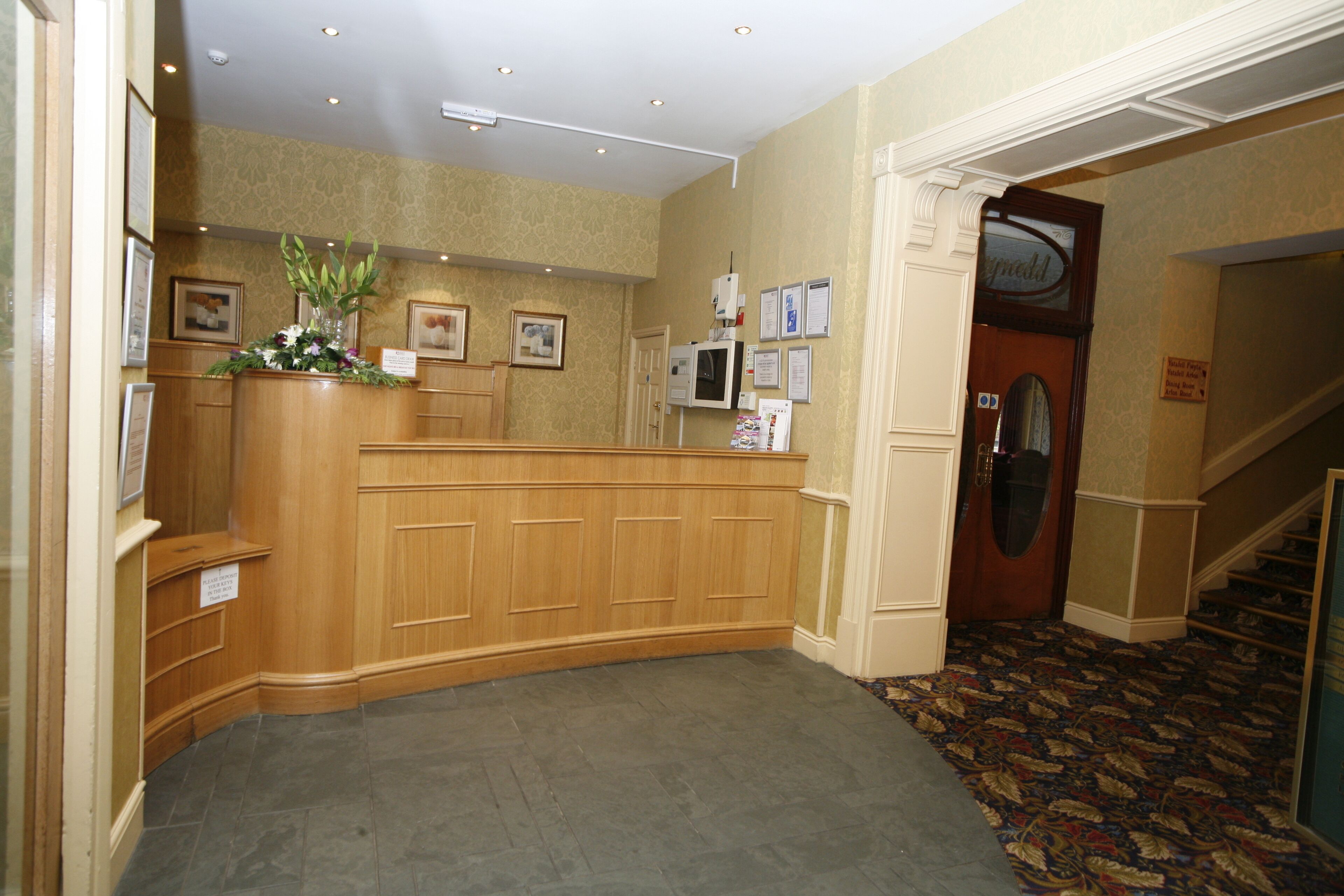 A reception area with a wooden desk, framed pictures on the wall, and a carpeted floor.