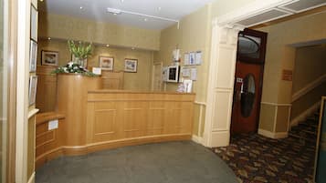 A reception area with a wooden desk, framed pictures on the wall, and a carpeted floor.