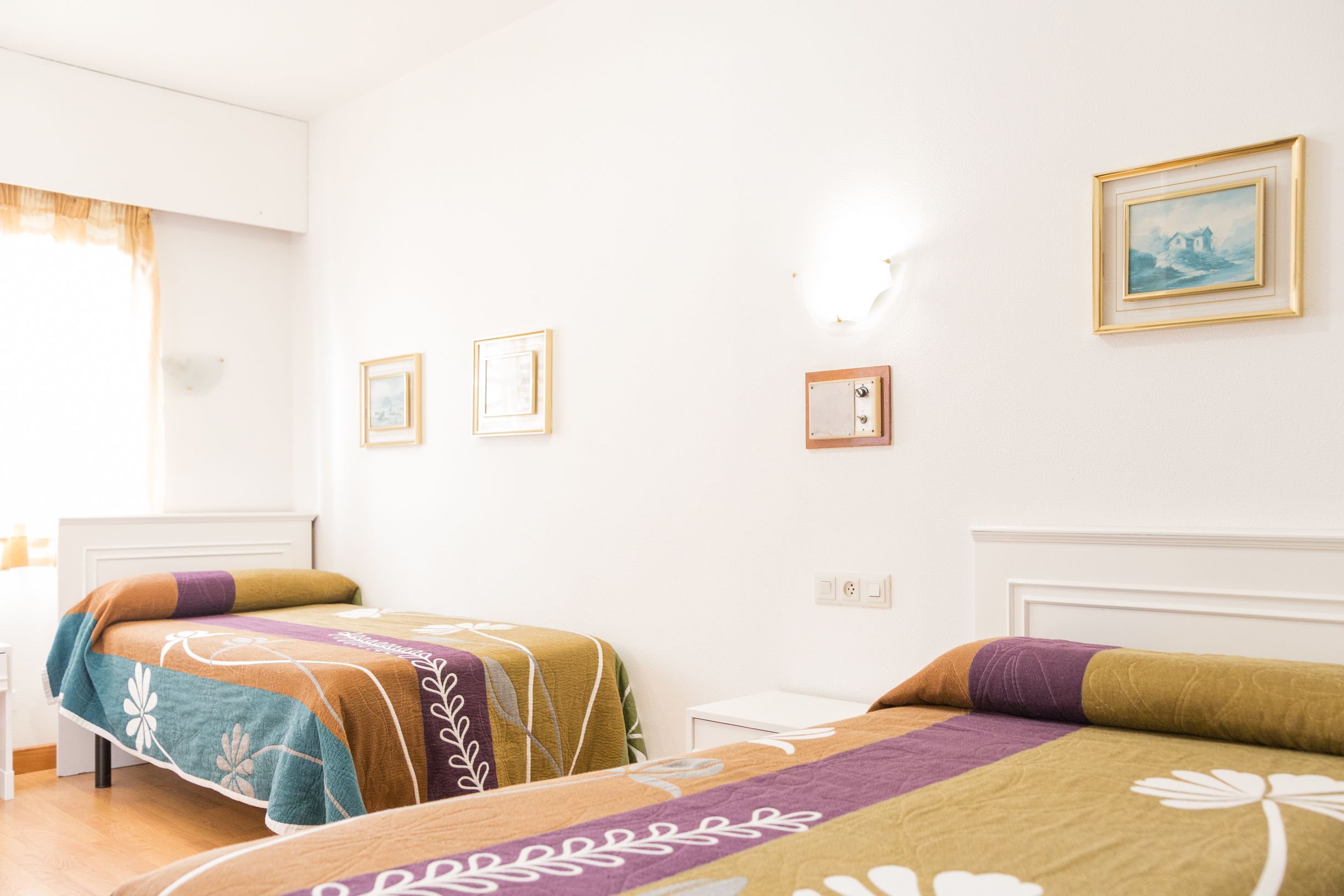 A hotel room with two beds, a small bedside table, and a wall-mounted light fixture.