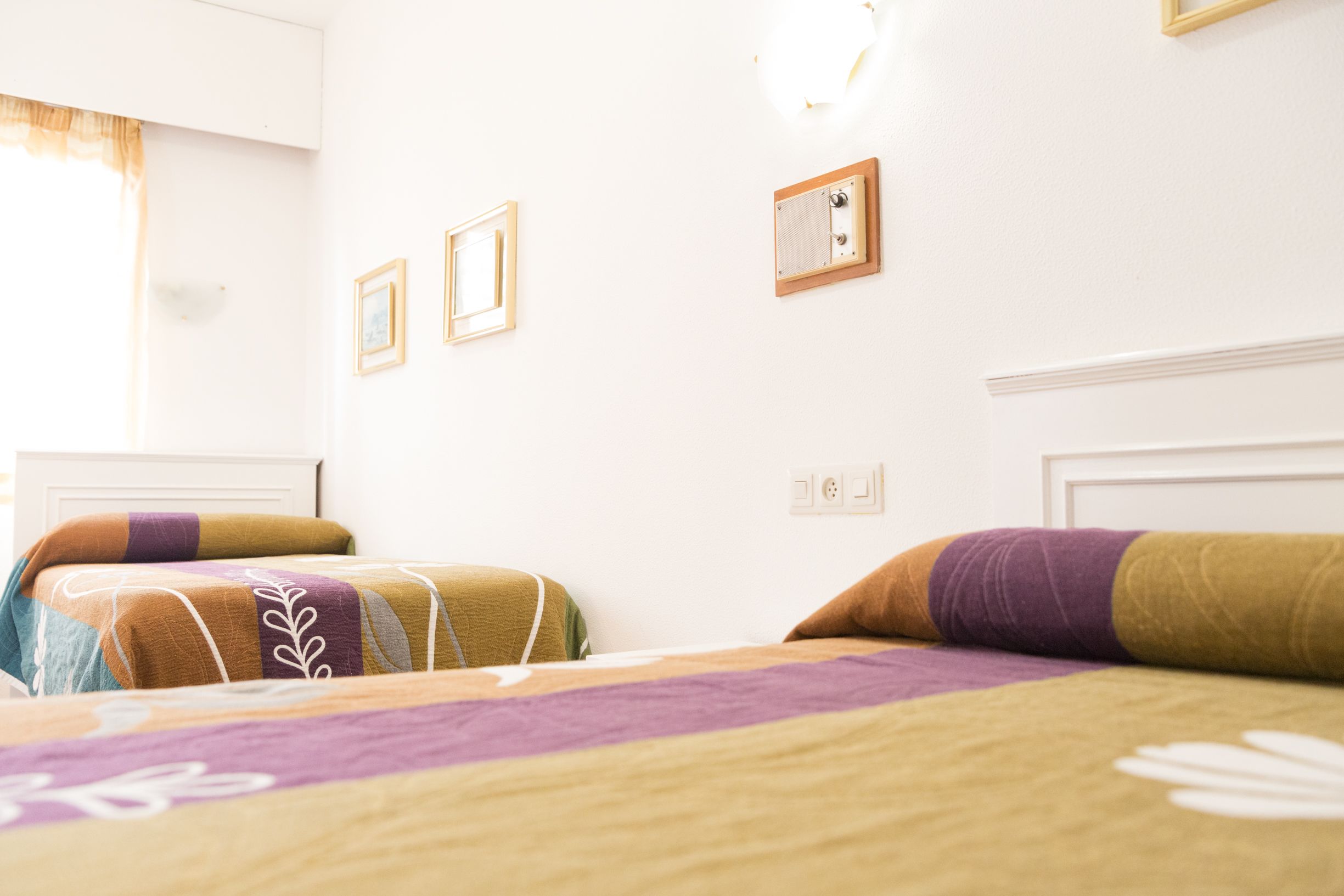 Ett hotellrum med två sängar, var och en med färgglatt sänglinne. Det finns väggmonterade ljusströmbrytare och en liten tavla på väggen.