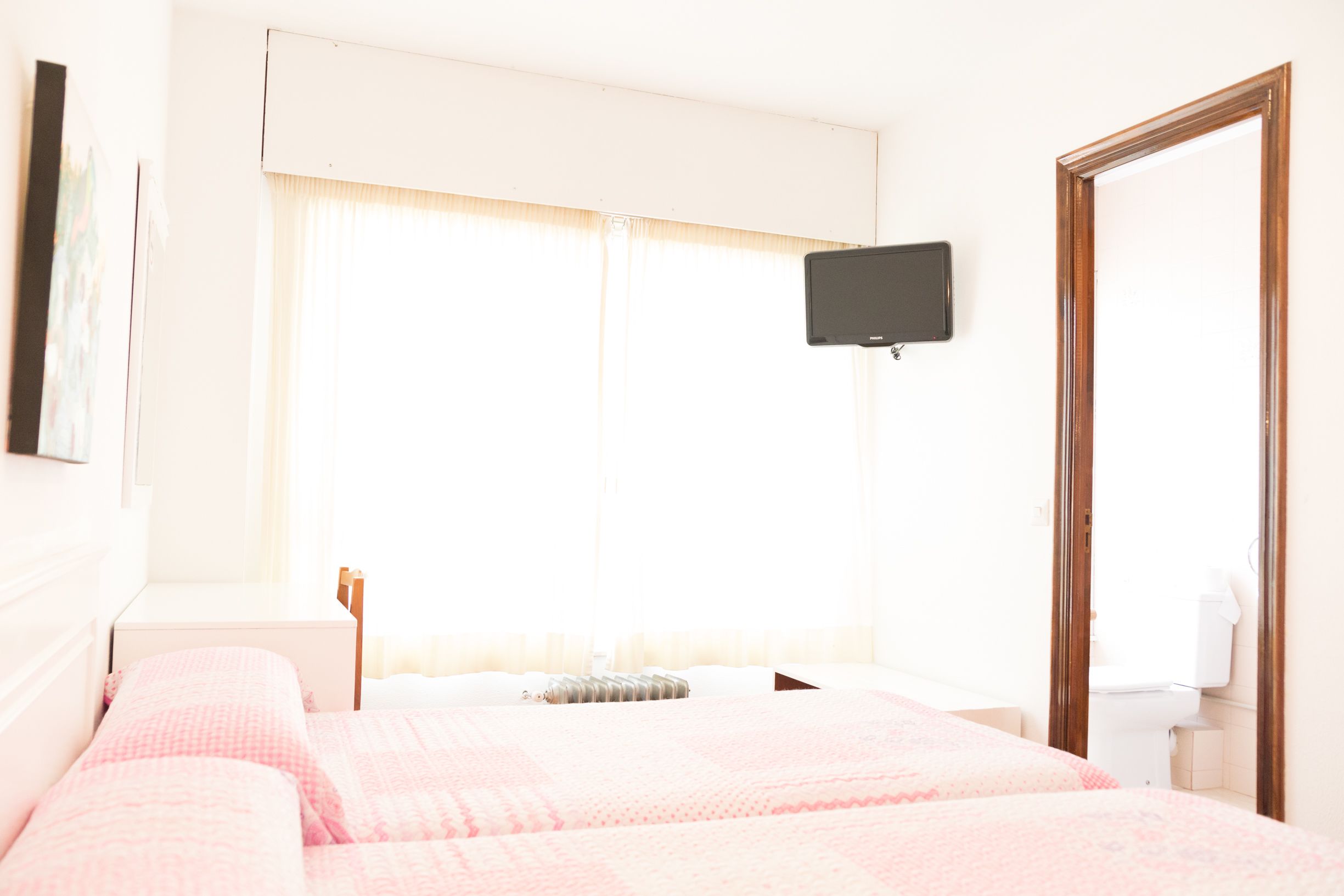 Een hotelkamer met een bed, een aan de muur bevestigde televisie en een raam met gordijnen.