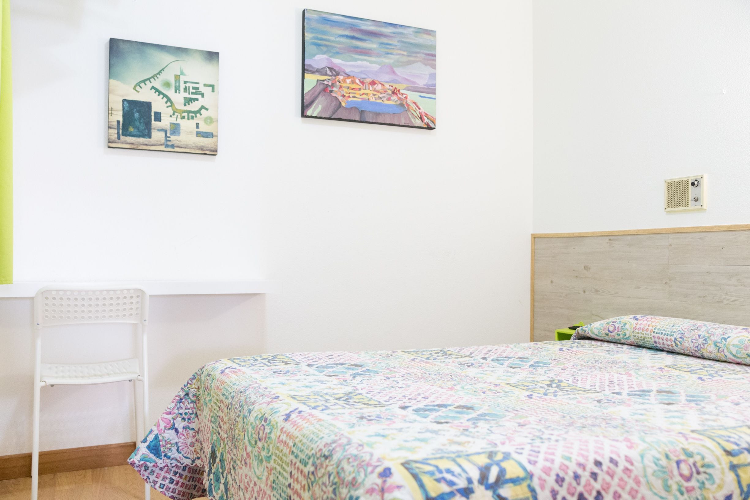 A bedroom with a bed, a chair, and two wall-mounted artworks.