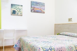 Un dormitorio con una cama, una silla y dos obras de arte en la pared.