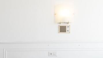 Una cama con colcha estampada, cabecero blanco y lámpara de pared.
