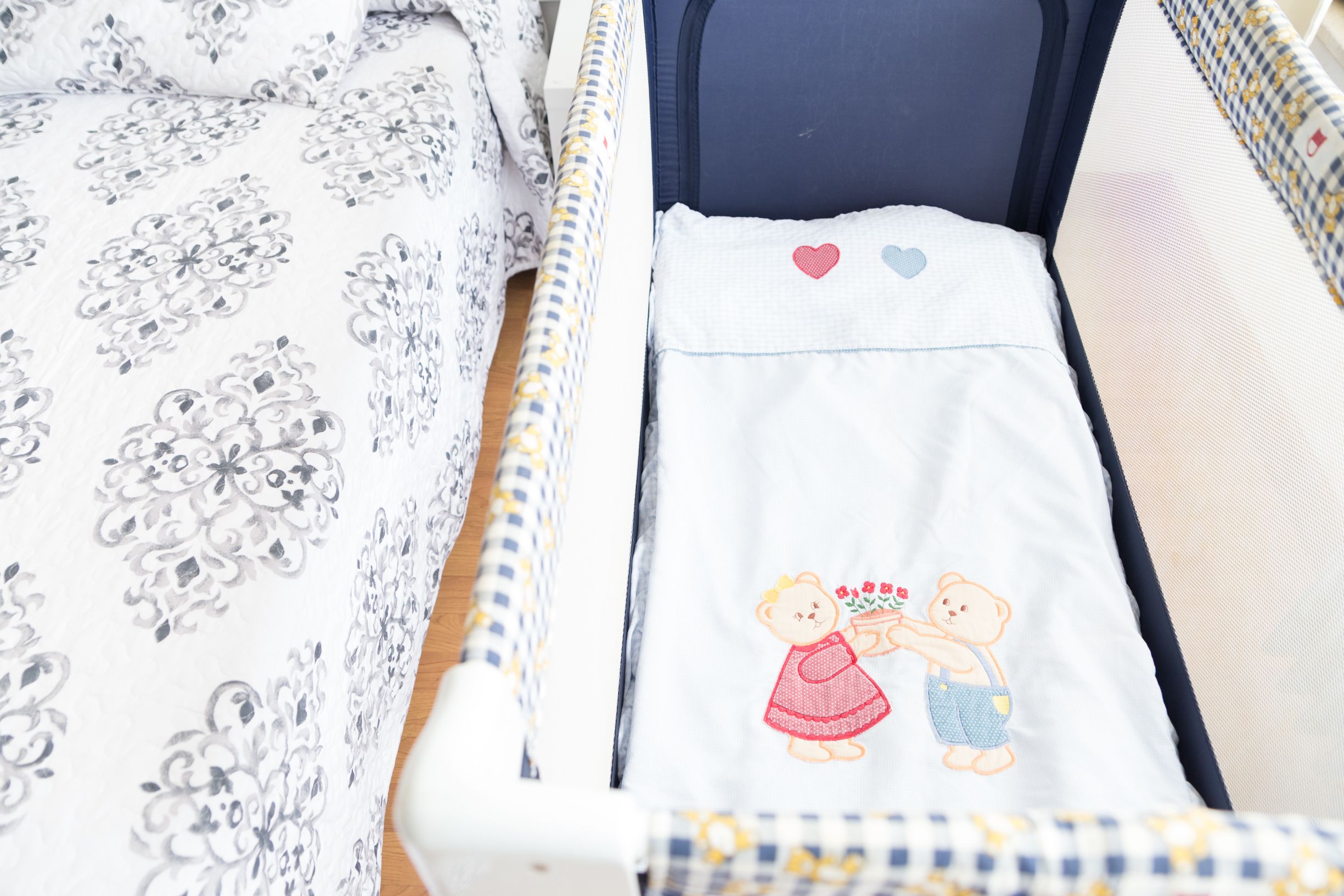 Una cuna con una colcha de motivos florales, una manta blanca con diseño de osito de peluche y un cabecero azul.