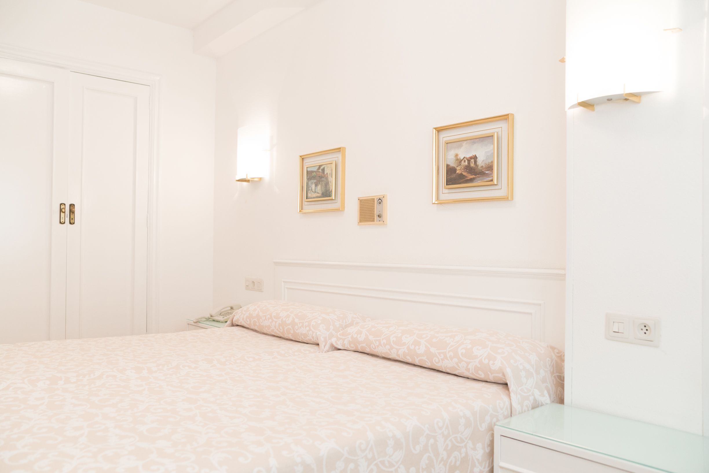 A bedroom with a bed, bedside tables, and two framed pictures on the wall.