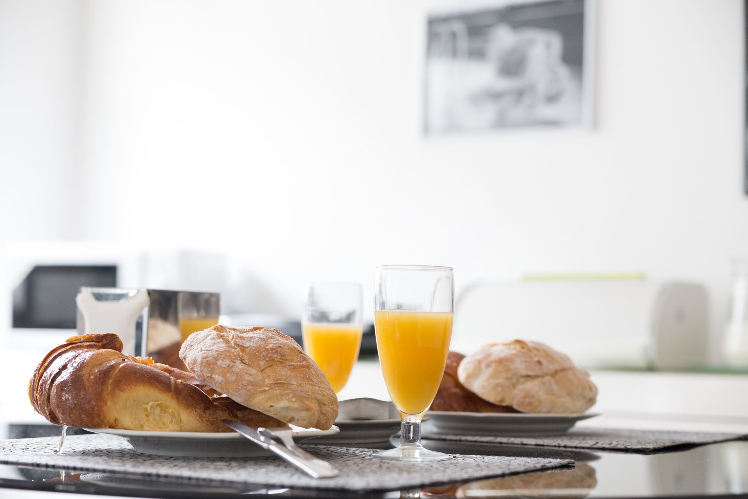 Una mesa con cruasanes, jugo de naranja y una cafetera.
