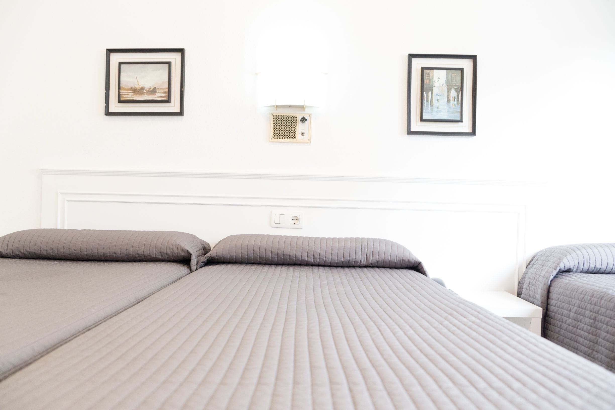 A hotel room with two beds, a white headboard, and two framed pictures on the wall.