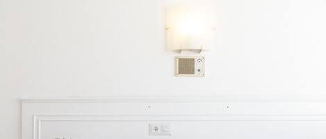 Una cama bien tendida con ropa de cama estampada, una lámpara de pared y un pequeño altavoz.