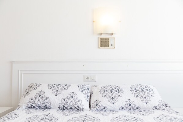 A neatly made bed with patterned bedding, a wall-mounted light fixture, and a small speaker.