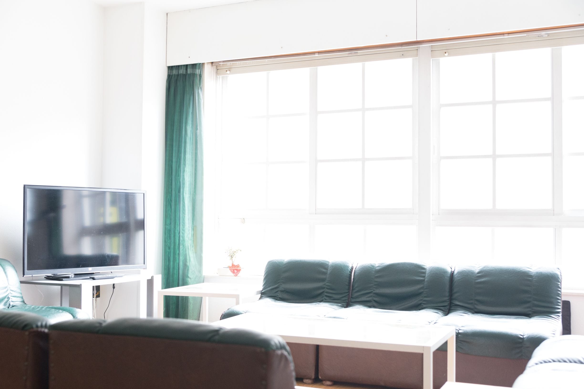 A modern living room with a flat-screen TV, a green sofa, and a window with curtains.