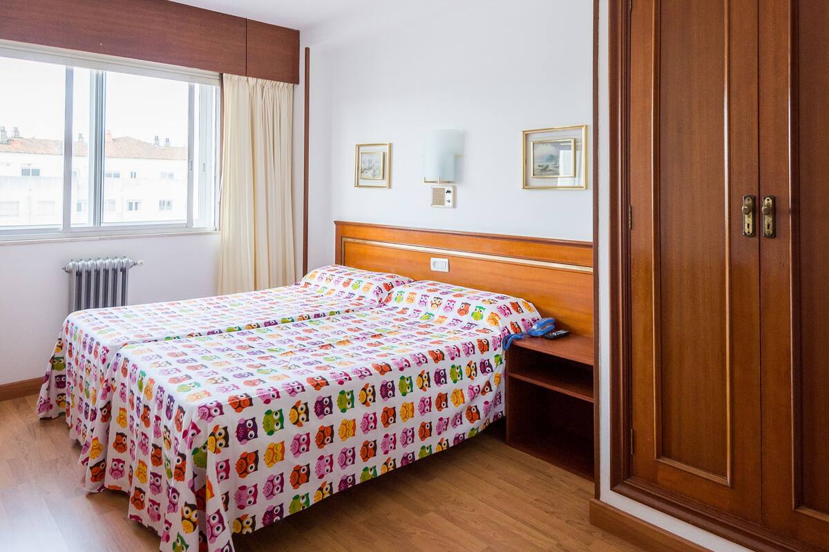 A hotel room with a large bed, a wardrobe, a bedside table, a window with curtains, and a radiator.