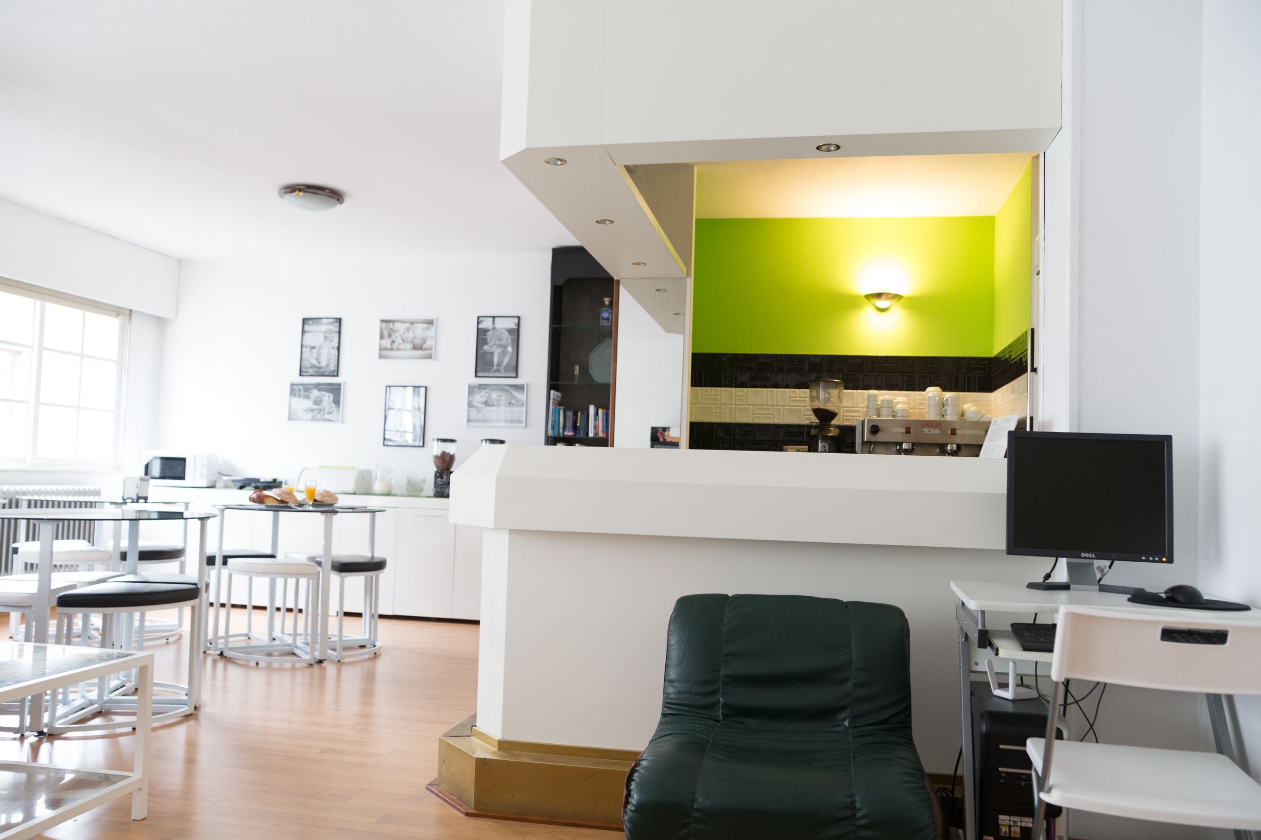 A modern kitchen with a green accent wall, a dining area with bar stools, and a computer desk with a monitor.